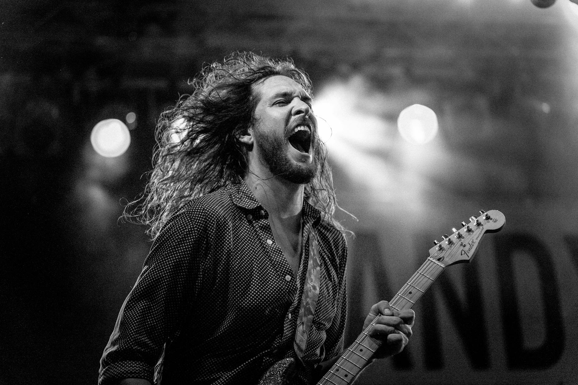 Artista con pelo largo cantando mientras sostiene la guitarra